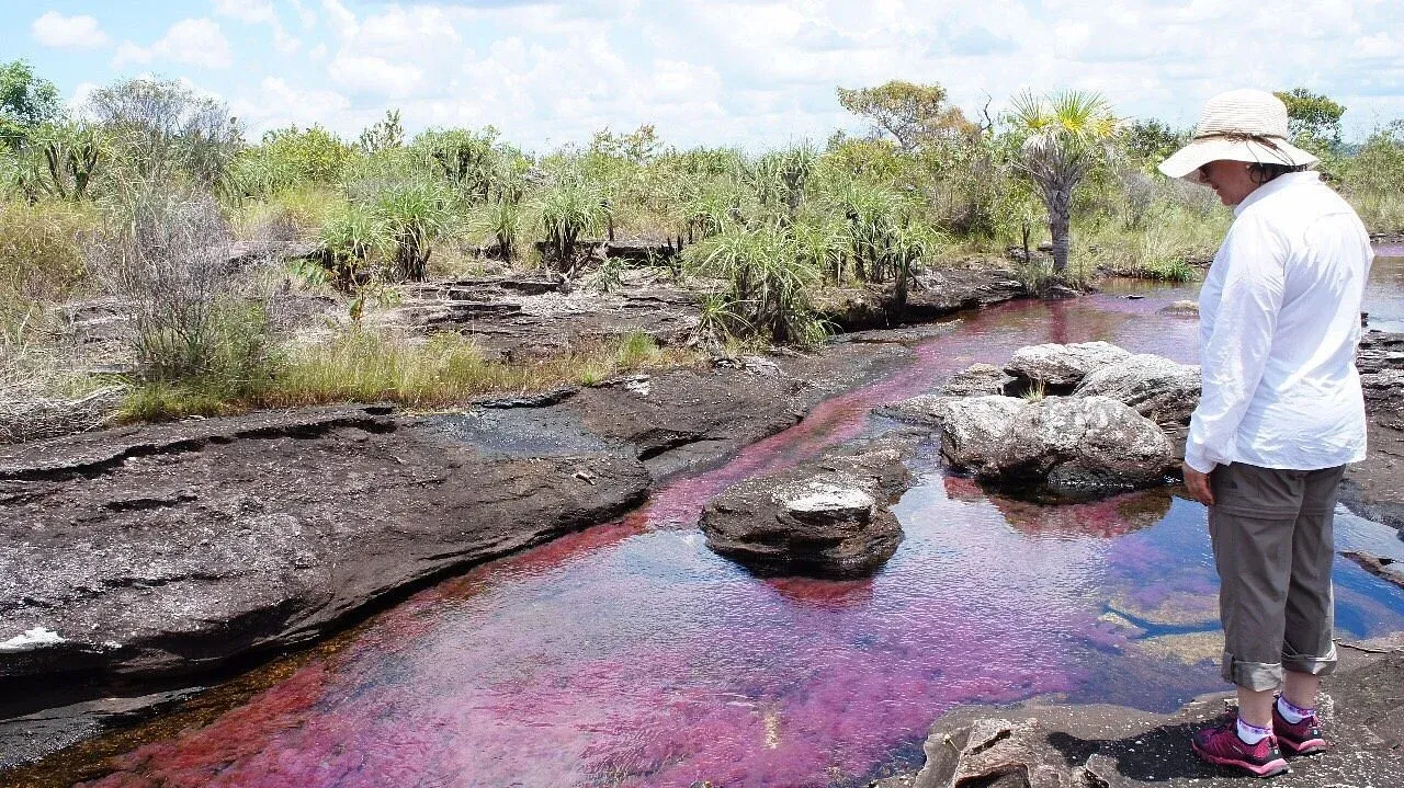 mujer parado sobre la orilla del río de 7 colores en Colombia.